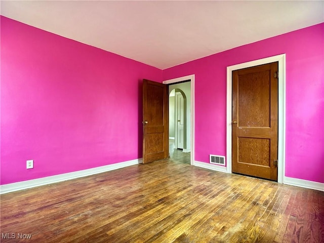 spare room with arched walkways, visible vents, baseboards, and wood finished floors