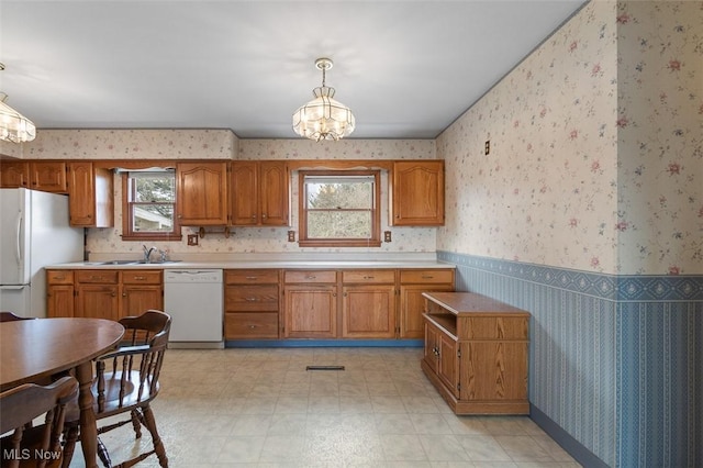 kitchen featuring white appliances, a wainscoted wall, wallpapered walls, light countertops, and brown cabinets