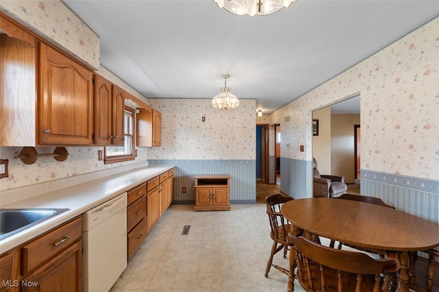 kitchen featuring brown cabinetry, a wainscoted wall, wallpapered walls, an inviting chandelier, and dishwasher