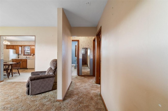 hall featuring wallpapered walls, baseboards, a chandelier, light colored carpet, and a sink