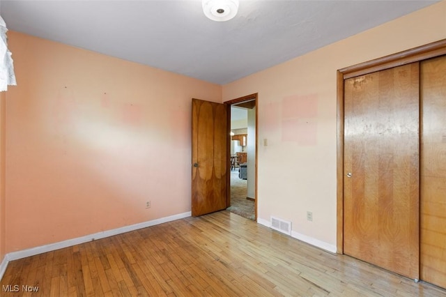 unfurnished bedroom with a closet, visible vents, baseboards, and hardwood / wood-style flooring