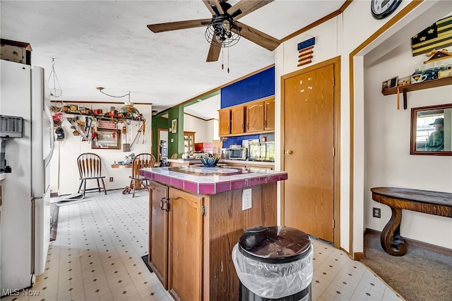 kitchen featuring a ceiling fan, freestanding refrigerator, baseboards, light floors, and tile counters