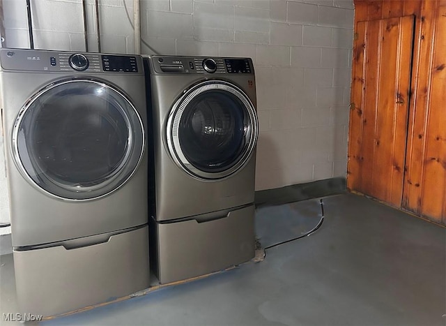 clothes washing area with concrete block wall, laundry area, and washing machine and clothes dryer