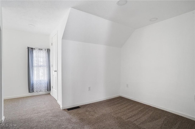 carpeted empty room with lofted ceiling, baseboards, and visible vents