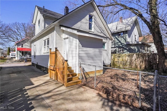 view of property exterior with driveway, a chimney, and fence