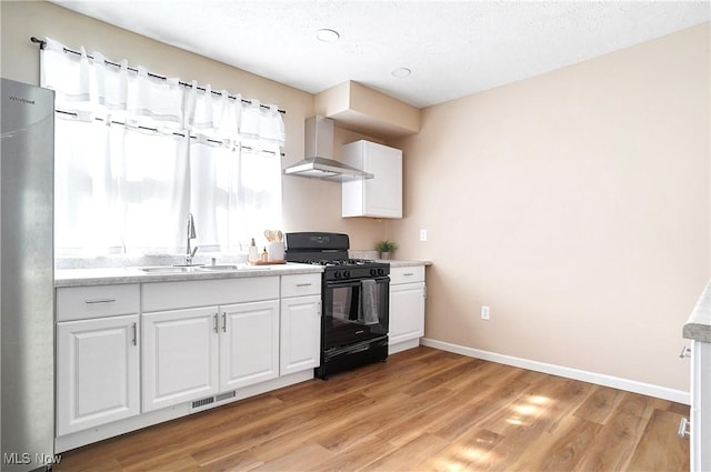 kitchen with visible vents, freestanding refrigerator, a sink, black range with gas stovetop, and wall chimney range hood