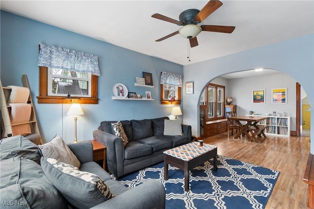 living area featuring ceiling fan, arched walkways, and wood finished floors