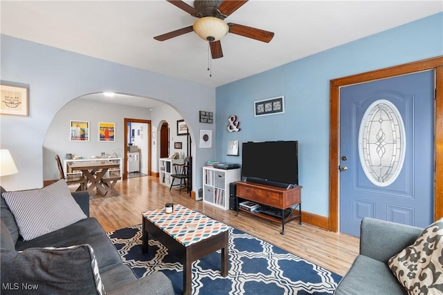 living area with baseboards, arched walkways, wood finished floors, and a ceiling fan