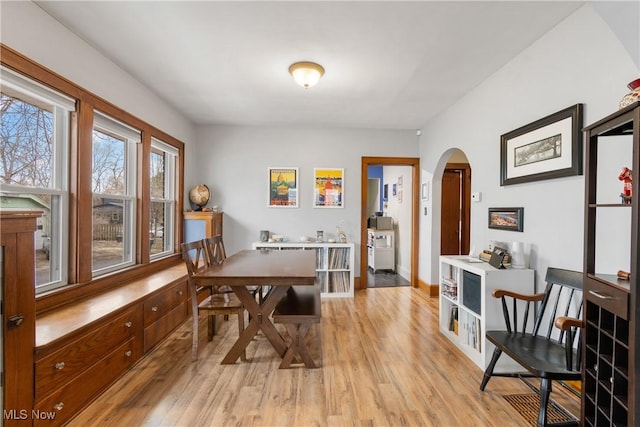 dining area with baseboards, arched walkways, and light wood-type flooring