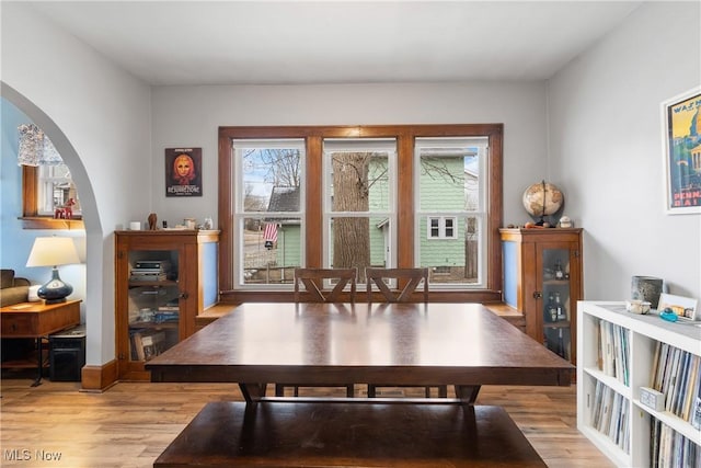 dining room with arched walkways, a healthy amount of sunlight, and light wood-style floors