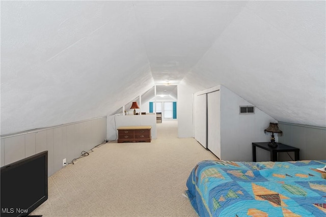 carpeted bedroom with visible vents, lofted ceiling, a closet, and wood walls