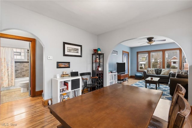 home office featuring ceiling fan, baseboards, arched walkways, and light wood-style flooring