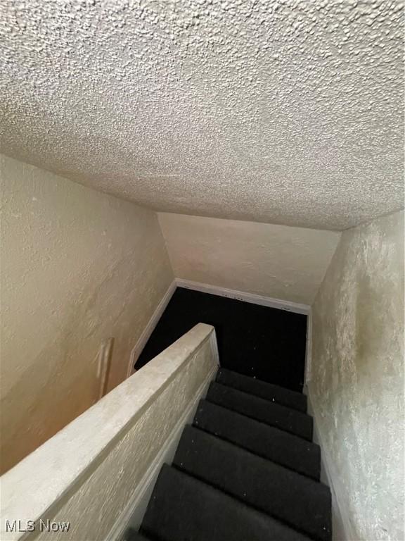 stairway featuring a textured ceiling, lofted ceiling, and a textured wall