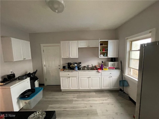 kitchen with white microwave, white cabinets, and freestanding refrigerator