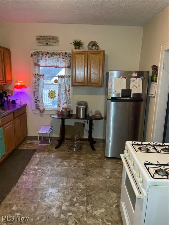 kitchen with a textured ceiling, white gas range, freestanding refrigerator, and brown cabinets