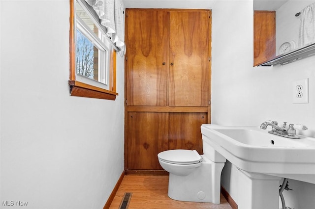 half bath featuring wood finished floors, visible vents, baseboards, a sink, and toilet