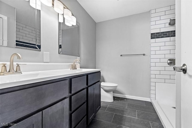 bathroom with toilet, a sink, a tile shower, double vanity, and baseboards