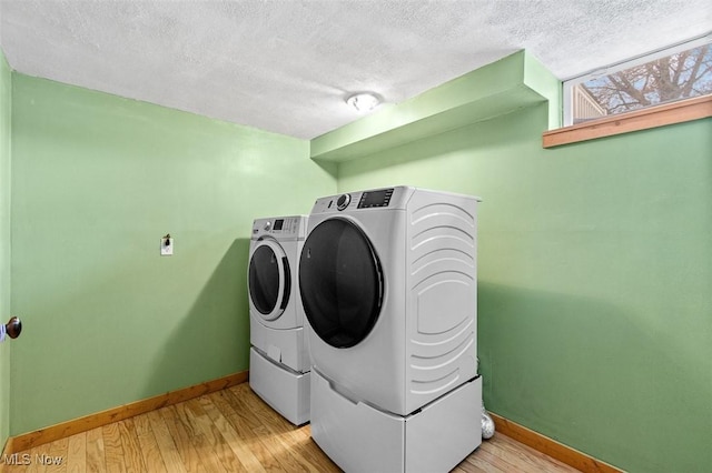 laundry area featuring washer and clothes dryer, a textured ceiling, light wood-style floors, baseboards, and laundry area