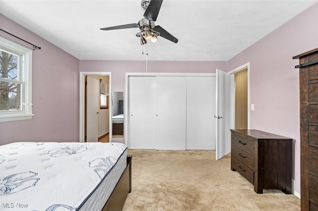 bedroom featuring light carpet, ensuite bath, a closet, and a ceiling fan