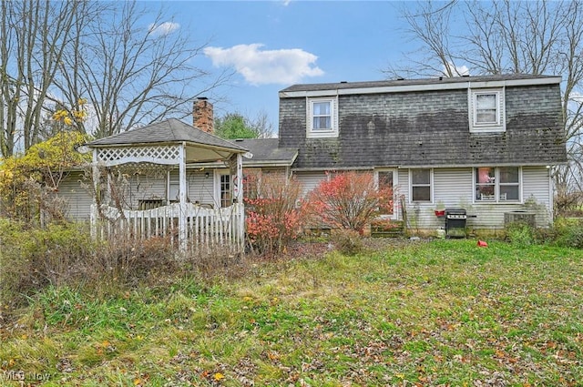 back of property with a lawn and roof with shingles