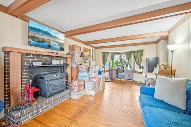 living room with beam ceiling, a wood stove, and wood-type flooring