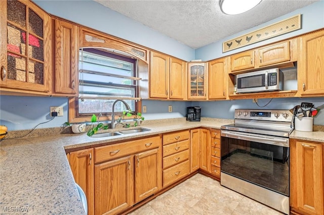 kitchen featuring glass insert cabinets, light countertops, stainless steel appliances, a textured ceiling, and a sink