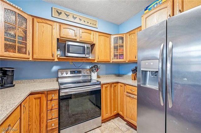 kitchen with glass insert cabinets, light stone counters, stainless steel appliances, light tile patterned flooring, and a textured ceiling