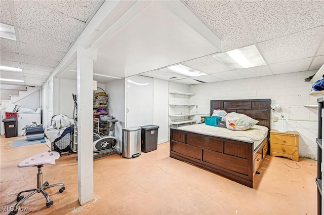 bedroom featuring a drop ceiling, concrete block wall, and concrete flooring