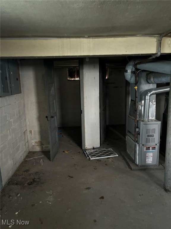 unfinished basement with heating unit, concrete block wall, and electric panel