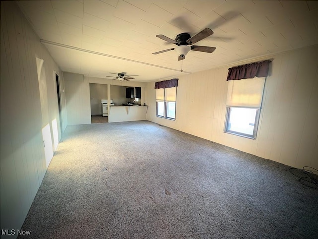 unfurnished living room featuring a ceiling fan, carpet, and wood walls