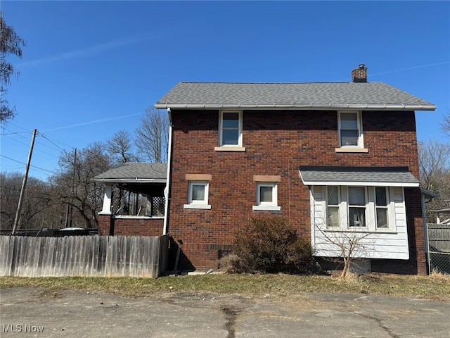 view of property exterior featuring brick siding, a shingled roof, a chimney, and fence