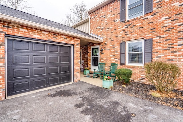 entrance to property featuring aphalt driveway, an attached garage, and brick siding