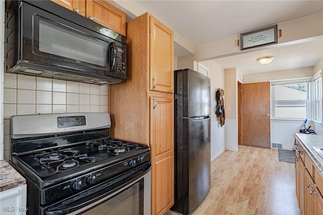 kitchen with light wood-type flooring, visible vents, a wainscoted wall, black appliances, and tasteful backsplash