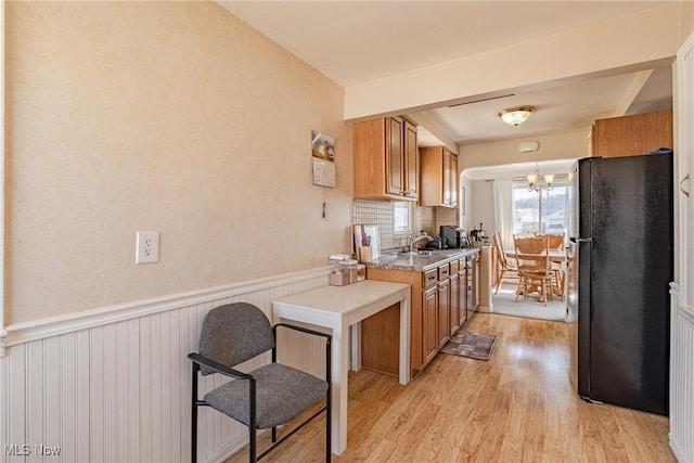 kitchen featuring light wood-type flooring, wainscoting, freestanding refrigerator, brown cabinetry, and a notable chandelier