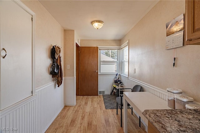 corridor with a wainscoted wall, visible vents, and light wood-style flooring