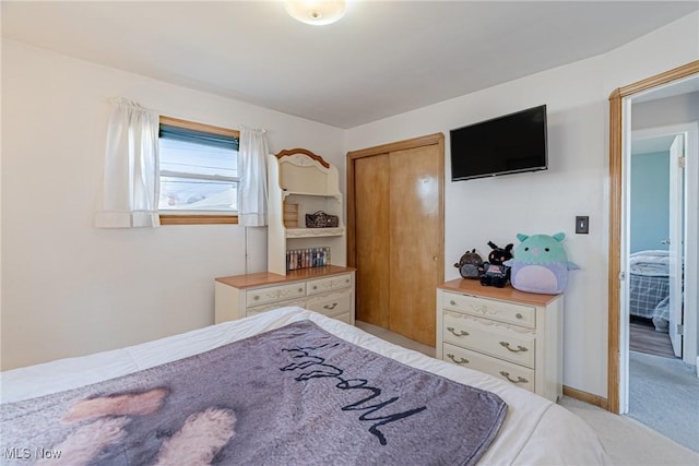 bedroom with a closet, light colored carpet, and baseboards