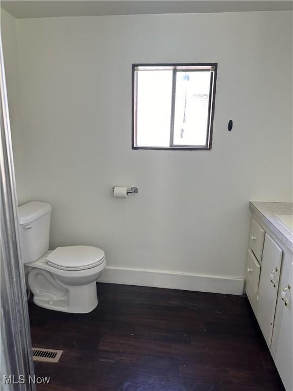 half bath featuring baseboards, toilet, wood finished floors, and vanity