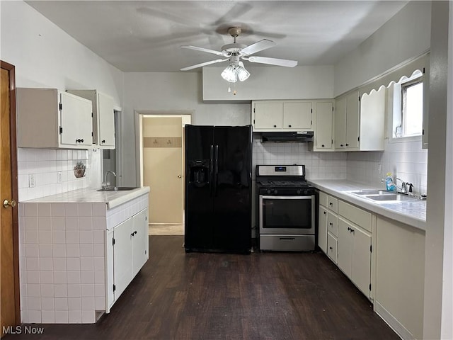 kitchen with under cabinet range hood, gas range, light countertops, black fridge, and a sink