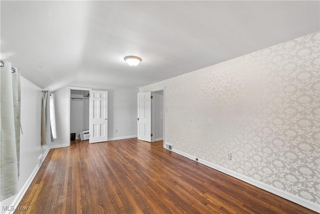 unfurnished bedroom featuring hardwood / wood-style floors, baseboards, wallpapered walls, vaulted ceiling, and a closet