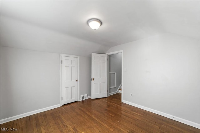 spare room featuring hardwood / wood-style floors, vaulted ceiling, visible vents, and baseboards