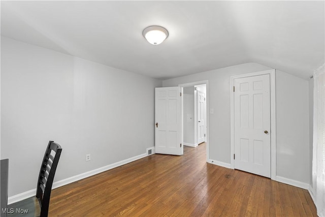 interior space featuring vaulted ceiling, visible vents, baseboards, and hardwood / wood-style flooring