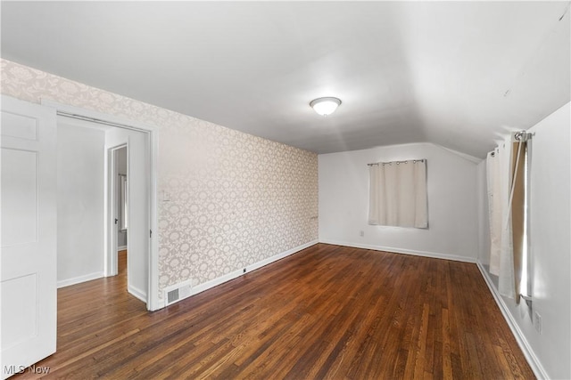 empty room with wallpapered walls, dark wood finished floors, visible vents, and baseboards