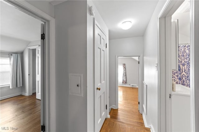 hall with visible vents, baseboards, and light wood finished floors