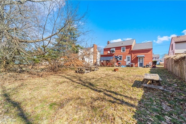 back of house featuring a lawn, a chimney, and fence