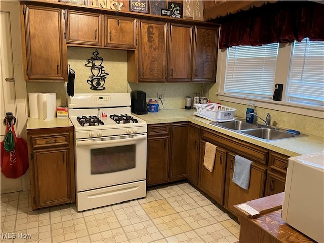 kitchen with a sink, light floors, white gas range oven, and light countertops