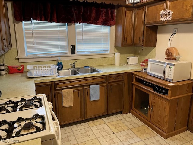 kitchen featuring light floors, white appliances, light countertops, and a sink