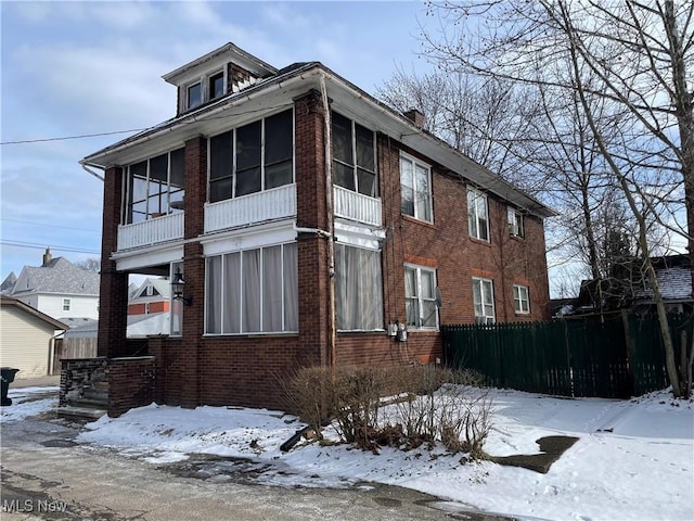 view of snow covered exterior featuring fence, brick siding, and a sunroom