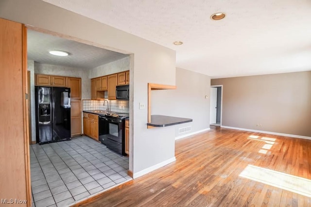 kitchen featuring visible vents, black appliances, a sink, dark countertops, and baseboards