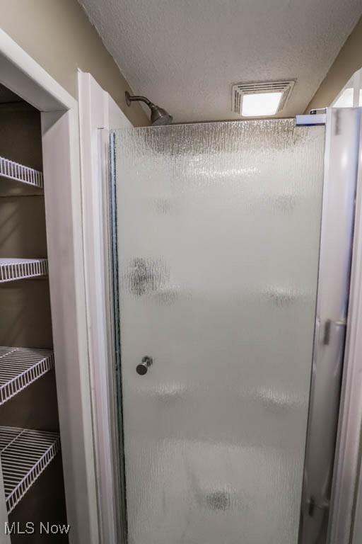 bathroom with visible vents, a textured ceiling, and a stall shower