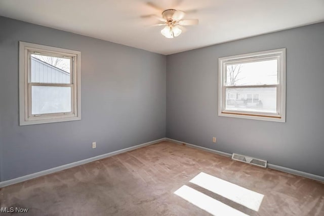 carpeted empty room featuring a wealth of natural light, visible vents, baseboards, and ceiling fan